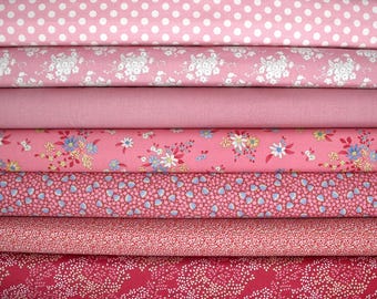 May include: A stack of pink fabric rolls with various patterns. The patterns include white polka dots, floral designs, and small repeating shapes. The fabrics range in shades from light to deep pink.