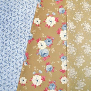 Op de afbeelding: Drie stoffen stalen met bloempatronen. Eén is lichtblauw met kleine, donkerblauwe stippen. De tweede is bruin met blauwe en witte rozen en roze accenten. De derde is bruin met kleine witte bloemen.