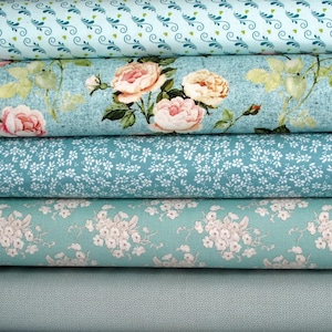 Könnte beinhalten: Ein Stapel Stoffrollen in Türkis- und Blautönen. Die oberste Rolle hat ein sich wiederholendes Muster aus grünen Blättern und Herzen. Die zweite Rolle zeigt große rosa Rosen. Andere Rollen zeigen Blumen- und Punktmuster. Die Stoffe scheinen aus Baumwolle zu sein.