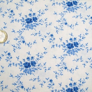 Può includere: Tessuto bianco con un motivo ripetuto di rose blu e tralci. Il disegno floreale è uniformemente distanziato. È visibile una moneta in euro, che funge da riferimento dimensionale.