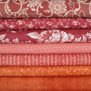Könnte beinhalten: Ein Stapel verschiedener roter und orangefarbener Stoffstücke. Die Stoffe weisen florale, gepunktete und gemusterte Designs auf. Einige Stoffe haben Text. Die Farbpalette umfasst Rot-, Korallen- und Orangetöne und schafft eine warme Ästhetik. Ideal für Quilt- und Nähprojekte.