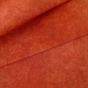 Può includere: Primo piano di un tessuto arancione testurizzato con un sottile motivo maculato. Il tessuto è piegato a metà, creando una piega al centro.