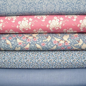 Könnte beinhalten: Eine Auswahl an Stoffrollen mit verschiedenen floralen und gemusterten Designs. Die Stoffe umfassen ein hellblaues Blumenmuster, einen rosa Stoff mit weißen Blumen, einen blauen Stoff mit Vögeln und Blumen, einen blauen Stoff mit kleinen weißen Punkten und einen einfarbigen blauen Stoff.