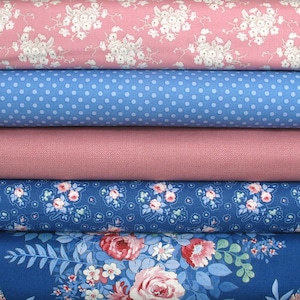 May include: A stack of five fabric bolts featuring various patterns. The top bolt is pink with white flowers, followed by a light blue bolt with white polka dots, a solid dusty pink bolt, a dark blue bolt with small flowers, and a dark blue floral print.