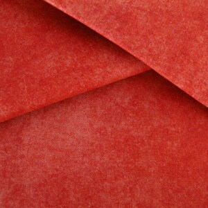 Op de afbeelding: Close-up van een rode stof met een textuur. De stof is gevouwen in een driehoekige vorm.