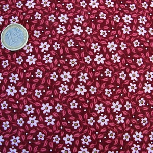 May include: Red fabric with a white floral pattern. The fabric is covered in small white flowers and leaves, with tiny white dots scattered throughout.