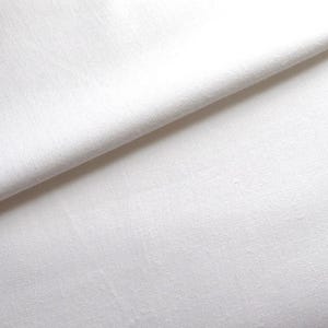 May include: A close-up of a white fabric with a smooth texture. The fabric is folded in half, creating a crease down the centre.