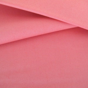 Peut inclure: Gros plan sur un tissu rose lisse avec une texture subtile. Le tissu est plié de manière à créer un aspect doux et fluide.