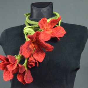 Puede incluir: Un collar de flores de fieltro rojo con hojas de fieltro verde. El collar se muestra en un maniquí negro.