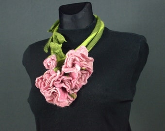Puede incluir: Un collar de flores de fieltro rosa con hojas de fieltro verde. El collar está en un maniquí negro.