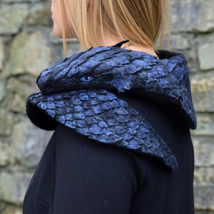 May include: A blue felt dragon head cowl with a blue eye. The cowl is worn around the neck and shoulders.