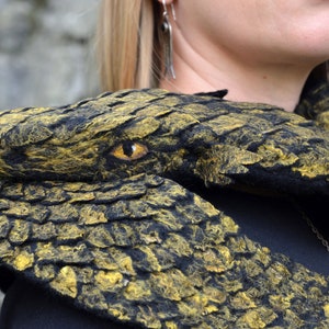May include: A black and gold felted snake scarf with a detailed eye. The scarf is made of wool and is a unique and stylish accessory.