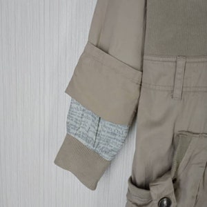 Peut inclure: Une veste beige avec une doublure &agrave; imprim&eacute; journal sur la manche. La veste a une poche &agrave; rabat sur le c&ocirc;t&eacute; droit et une fermeture &agrave; bouton.