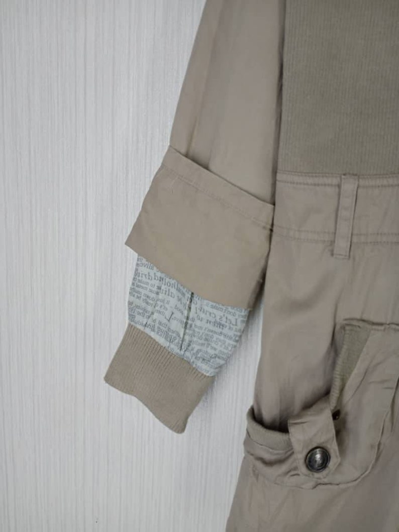 Peut inclure: Une veste beige avec une doublure &agrave; imprim&eacute; journal sur la manche. La veste a une poche &agrave; rabat sur le c&ocirc;t&eacute; droit et une fermeture &agrave; bouton.