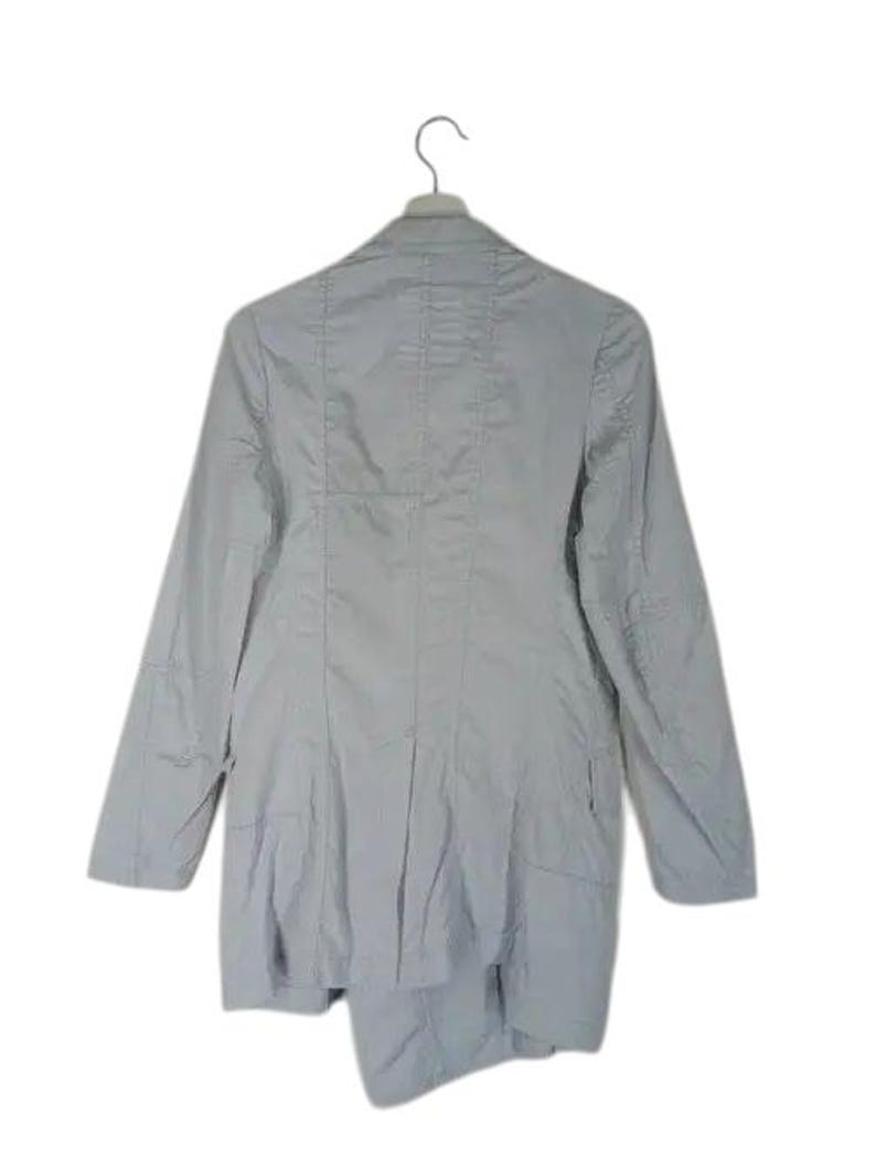 May include: A light gray blazer with long sleeves, hanging from a metal hanger. The blazer has a tailored fit with seams and a slightly asymmetrical hemline. The fabric appears to be a lightweight material.