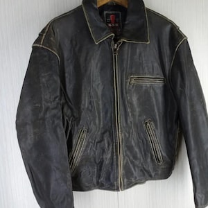 May include: A distressed black leather jacket with a zip-up front, a collared neckline, and multiple pockets. The jacket has a worn, vintage appearance with visible wear and tear, and is hanging from a wooden hanger.