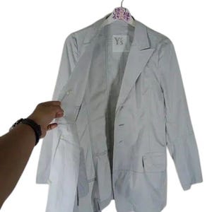 May include: A light gray blazer with a two-button closure, two front pockets, and a notched lapel. The jacket is hanging on a hanger with the text "BEST VINTAGE STORE" and the brand "Y's".