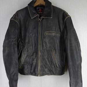 May include: A vintage black leather jacket with a zip-up front, two front pockets, and a collared neckline. The jacket shows signs of wear, with a distressed appearance and a faded color. The jacket is hanging on a wooden hanger.