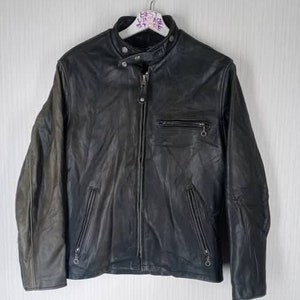 May include: Black leather jacket with a zip-up front, a small pocket on the chest, and two zippered pockets at the waist. The jacket has a classic biker style with a stand-up collar and a slightly worn appearance.