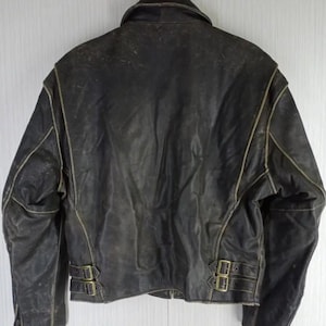 May include: A distressed black leather jacket with a classic design. The jacket features a notched collar, a zipper closure, and two adjustable waist straps with buckles. The seams are highlighted with a lighter color, and the leather shows signs of wear.