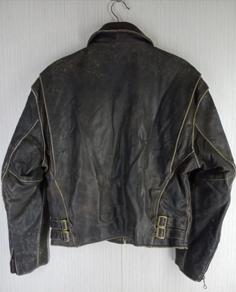 May include: A distressed black leather jacket with a classic design. The jacket features a notched collar, a zipper closure, and two adjustable waist straps with buckles. The seams are highlighted with a lighter color, and the leather shows signs of wear.