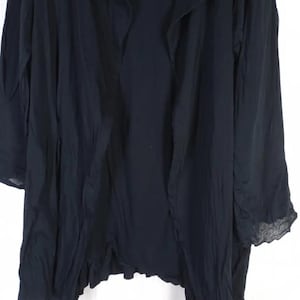 Op de afbeelding: Een lange, zwarte jas met een gedrapeerde kraag en lange mouwen. De stof lijkt licht van gewicht en heeft een licht gekreukte textuur. De zoom heeft een subtiele, gerimpelde rand, wat een vleugje detail aan het kledingstuk toevoegt.