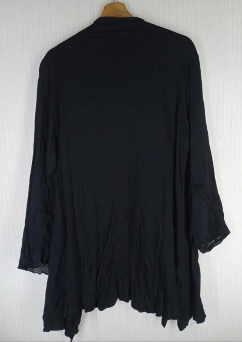 Op de afbeelding: Zwart top met lange mouwen en een asymmetrische zoom. Het kledingstuk is gemaakt van een lichte stof en hangt aan een houten hanger. De mouwen hebben een uitlopend ontwerp en de algehele stijl is los en relaxed.