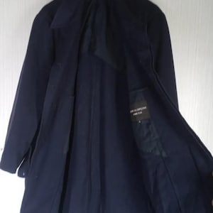 Pu&ograve; includere: Un cappotto blu navy dal design classico, appeso a una gruccia di legno. Il cappotto ha un colletto a revers, maniche lunghe e chiusura con bottoni. La fodera interna &egrave; visibile, con una piccola etichetta.