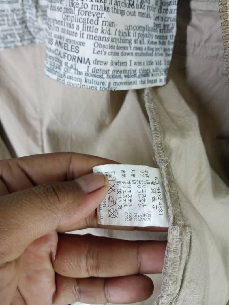 Peut inclure: Une &eacute;tiquette de v&ecirc;tement beige avec du texte noir et une &eacute;tiquette d'entretien blanche. L'&eacute;tiquette comprend le texte "NO. 9422-4381" et une liste de mat&eacute;riaux et de pourcentages. L'&eacute;tiquette d'entretien comprend des symboles pour le lavage, le repassage et le nettoyage &agrave; sec.
