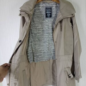 Peut inclure: Une veste beige &agrave; manches longues avec une fermeture &eacute;clair et une grande poche sur le c&ocirc;t&eacute; gauche. La veste est doubl&eacute;e d'un imprim&eacute; journal avec le texte "Von Dutch" et "Original Style" r&eacute;p&eacute;t&eacute; sur toute la surface.