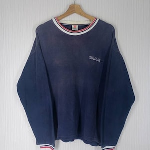 Könnte beinhalten: Ein marineblaues Langarmshirt mit einem weiß-rot gestreiften Kragen und Bündchen. Das Shirt hat ein kleines rotes Logo auf der linken Brust und das Wort "YALE" ist auf der Vorderseite gestickt.