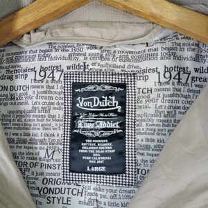 Peut inclure: Une veste beige avec un motif &agrave; carreaux noir et blanc. La veste porte une &eacute;tiquette qui dit "Von Dutch Love Addict" et comprend le texte "The noisiest, hottest, wildest, greatest sounds from the drag strip 110% Pure California Est. 1947".