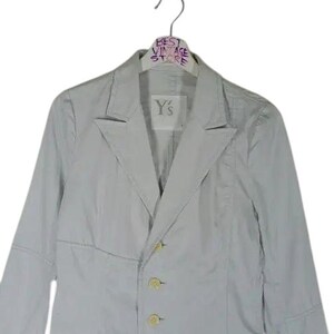 May include: A light gray blazer with three buttons and two pockets. The blazer is hanging on a hanger with the text "BEST VINTAGE STORE". The label on the blazer reads "Y's".