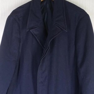 Pu&ograve; includere: Un cappotto blu navy in lana dal design classico. Il cappotto presenta un risvolto a lancia, una chiusura con bottoni e una lunghezza lunga. Il cappotto &egrave; appeso a un'appendiabiti di legno.