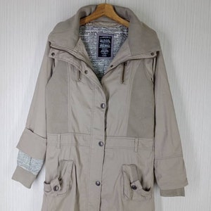 Peut inclure: Une veste beige &agrave; manches longues avec un col montant, une fermeture &eacute;clair et plusieurs poches. La veste est doubl&eacute;e d'une doublure imprim&eacute;e avec le texte "1947" et "Love & Luck".