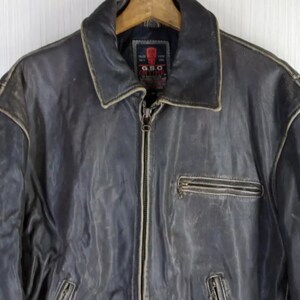 May include: A distressed, dark gray leather jacket with a zip-up front and multiple pockets. The jacket features a classic collar and a weathered appearance, suggesting vintage styling. The G.S.C. brand label is visible on the inside.