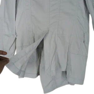 May include: A light gray jacket with a tailored design. The jacket features a button closure, multiple pockets, and a split hem. The fabric appears to be lightweight, suitable for transitional weather.