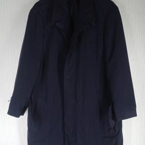 Pu&ograve; includere: Un cappotto blu navy con colletto a revers e due tasche anteriori. Il cappotto &egrave; appeso a una gruccia di legno su uno sfondo bianco. Il cappotto sembra essere fatto di un tessuto pesante.