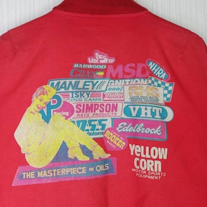May include: Red jacket with a vintage racing theme. The back features a colorful graphic with logos like MSD, Crane Cams, Manley, Isky, Simpson, VHT, Edelbrock, Hooker Headers, and Yellow Corn Motor Sports Equipment. The text "The Masterpiece in Oils" is also included.