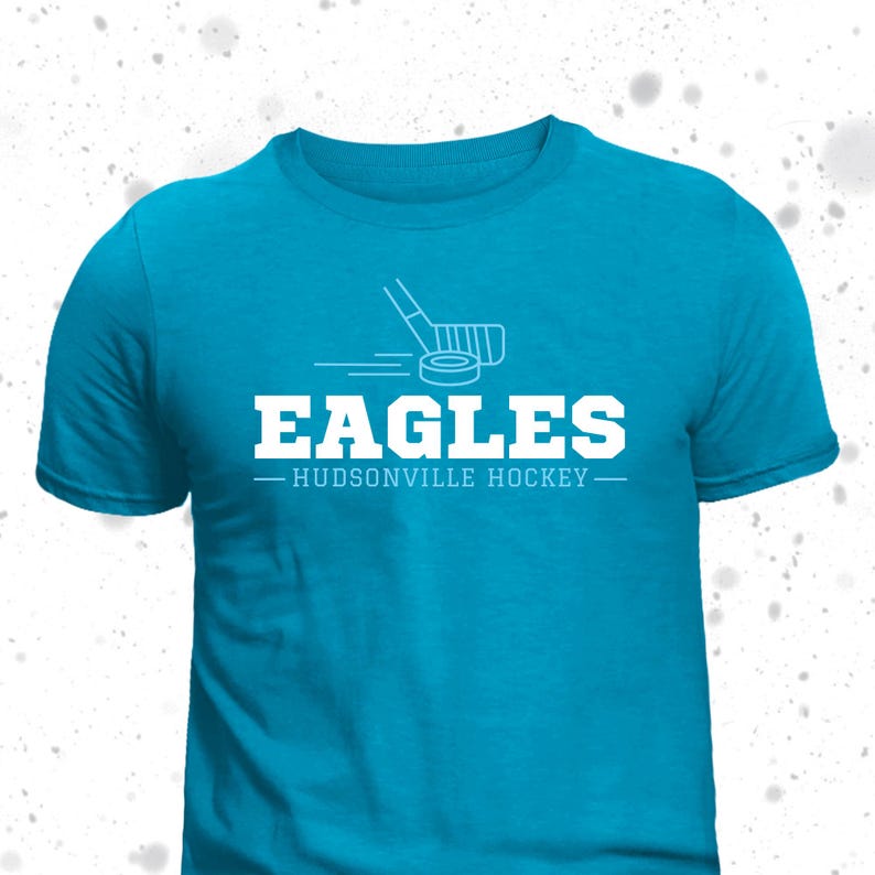May include: A turquoise blue t-shirt with a white hockey stick and puck graphic. The text "EAGLES - HUDSONVILLE HOCKEY -" is printed in white on the shirt.