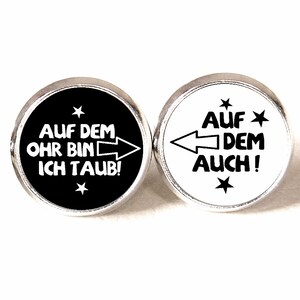 Könnte beinhalten: Ein Paar runde, silberne Ohrringe mit schwarzen und weißen Designs. Der schwarze Ohrring sagt "AUF DEM OHR BIN ICH TAUB!" mit einem weißen Pfeil, der nach rechts zeigt. Der weiße Ohrring sagt "AUF DEM AUCH!" mit einem schwarzen Pfeil, der nach links zeigt.
