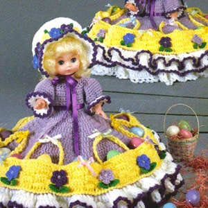 May include: Crochet pattern for a doll outfit and a basket in a yellow and purple colour scheme. The doll is wearing a purple dress with a white hat and a yellow skirt with purple flowers. The basket is filled with colourful eggs.