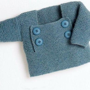 Puede incluir: Un cárdigan de bebé tejido en color verde azulado apagado. El cárdigan presenta un diseño clásico con cuello vuelto y tres botones a juego. La manga es visible en el lado izquierdo. La prenda está hecha de un hilo texturizado.