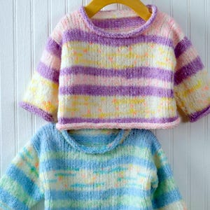 Puede incluir: Dos suéteres de punto a rayas para bebés, uno en rayas moradas, rosas y amarillas, y el otro en rayas azules, verdes y blancas.