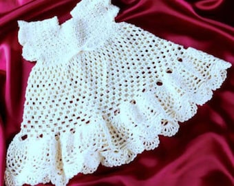 May include: A white crocheted baby dress with a scalloped hem and a delicate lace design.