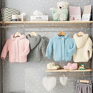 Può includere: Quattro maglioni di lana per neonati appesi a un rack. I maglioni sono rosa, grigio, azzurro e crema. I maglioni hanno cappucci e chiusura con bottoni. I maglioni sono appesi in una nursery o in una cameretta.