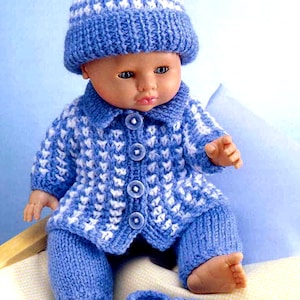 May include: A baby doll wearing a blue and white knitted outfit, including a hat with a white pom-pom, a button-down jacket, pants, and matching booties. The outfit is a cozy, handmade design.