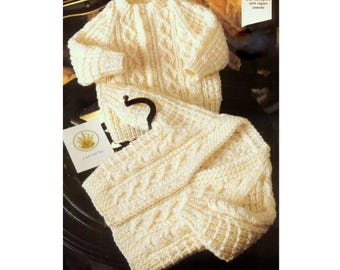 May include: A cream-colored knitted baby cardigan and matching pants with a cable knit pattern. The cardigan has a button closure at the neck and raglan sleeves. Sizes 45-60cm.