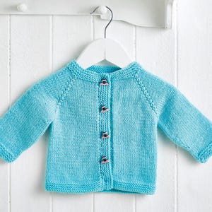 May include: A light blue knitted baby cardigan with long sleeves, displayed on a white hanger. The cardigan has a round neckline and is fastened with four small, decorative buttons. The garment is made of a soft, textured yarn.