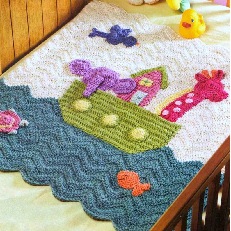 May include: A crocheted baby blanket with a white background and a blue, green, and pink design. The blanket features a crocheted ark with a giraffe, elephant, and bird on top. The ark is floating on a blue and green wave pattern.